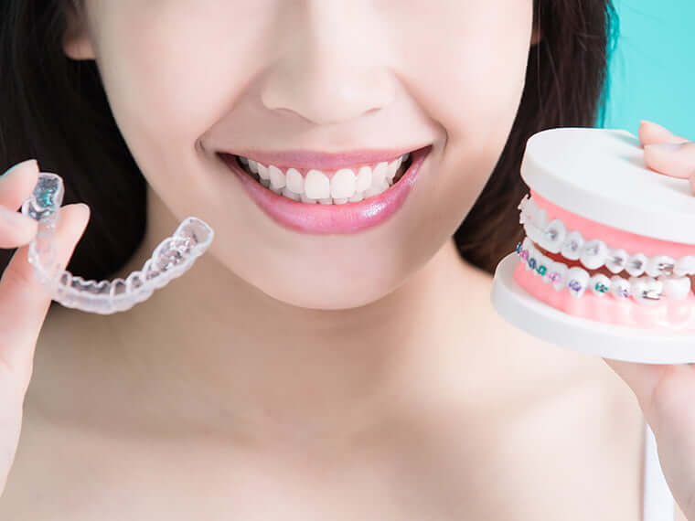 woman holding up a pair of clear aligners and a model of teeth with braces